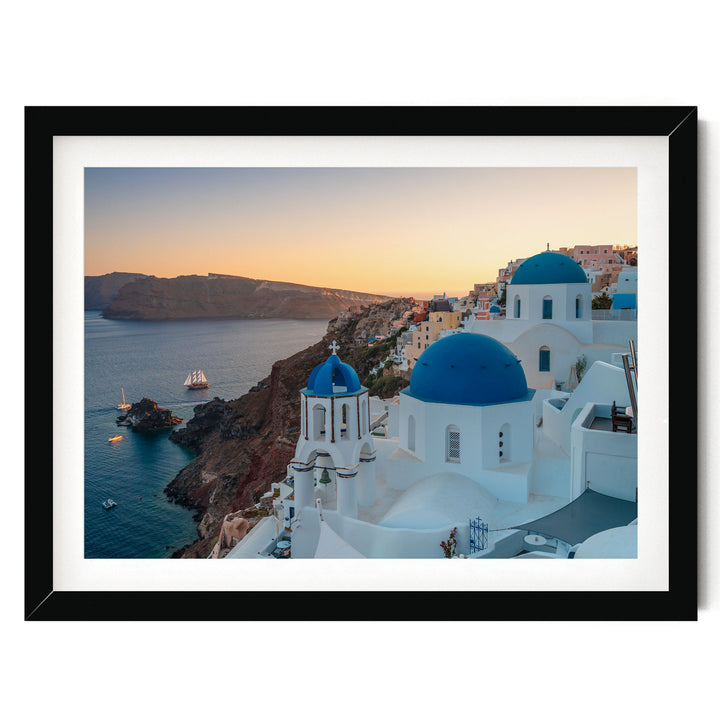 a picturesque coastal town with white buildings and blue domes, overlooking the ocean. The town is situated on a cliff, with a clear blue sky and a warm sunset in the background.