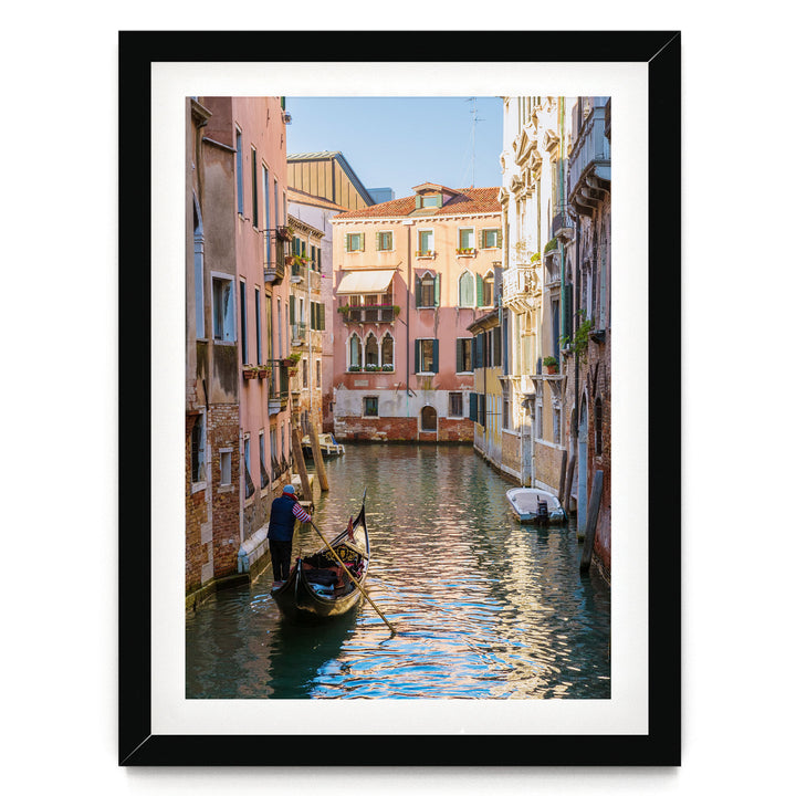 A gondolier navigates a traditional Venetian gondola through a picturesque canal, surrounded by colorful buildings and reflecting the clear blue sky.