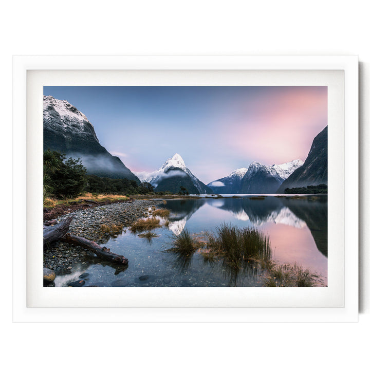 a serene landscape with a mountain range in the background, a calm lake in the foreground, and a clear blue sky with a pinkish-orange hue.