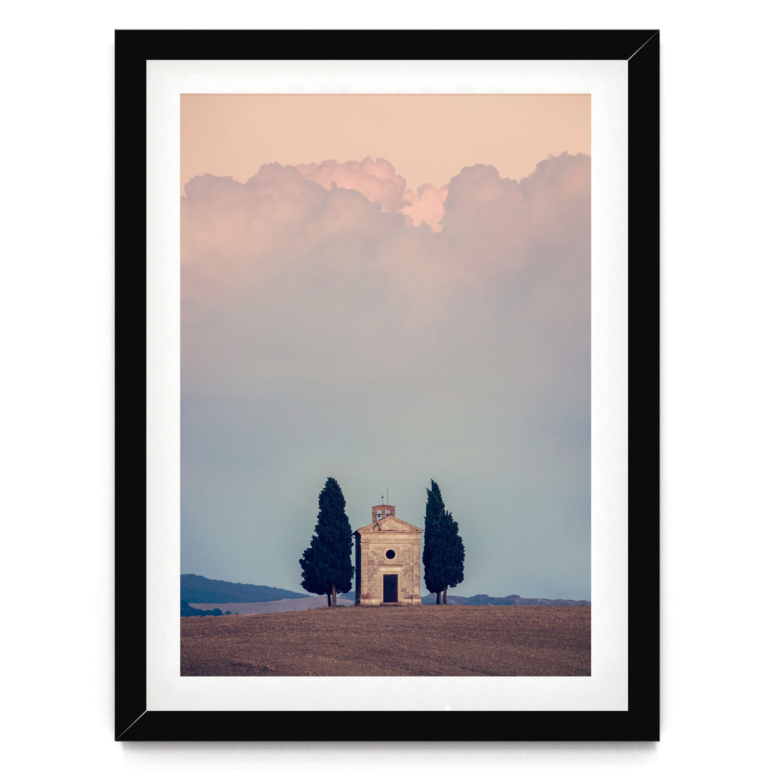 A framed image depicting a small stone church with a bell tower, surrounded by two tall cypress trees, set against a cloudy sky.