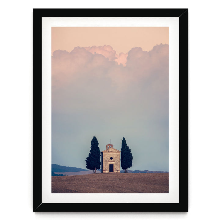 A framed image depicting a small stone church with a bell tower, surrounded by two tall cypress trees, set against a cloudy sky.