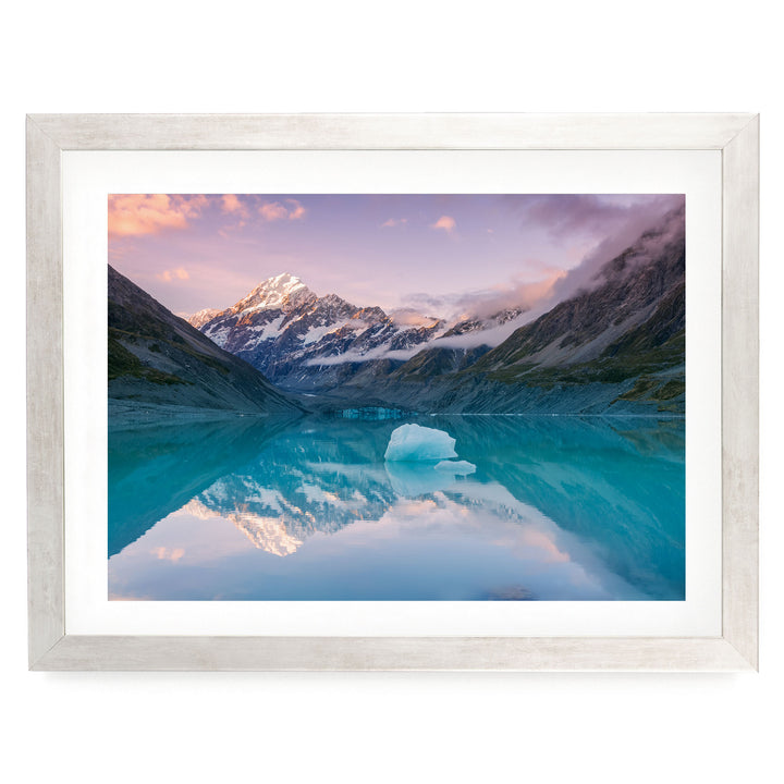 A breathtaking landscape featuring a serene lake with a majestic mountain range reflected in its calm waters, set against a stunning sky with vibrant hues of pink and purple.