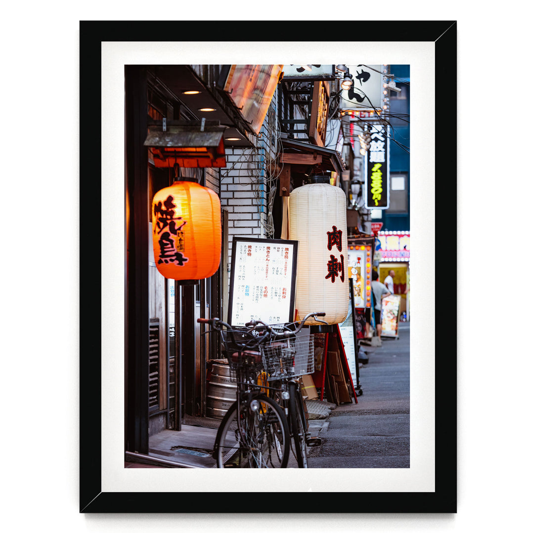 A bicycle parked on a street in front of a row of shops with colorful lanterns hanging above them.