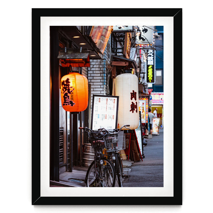 A bicycle parked on a street in front of a row of shops with colorful lanterns hanging above them.