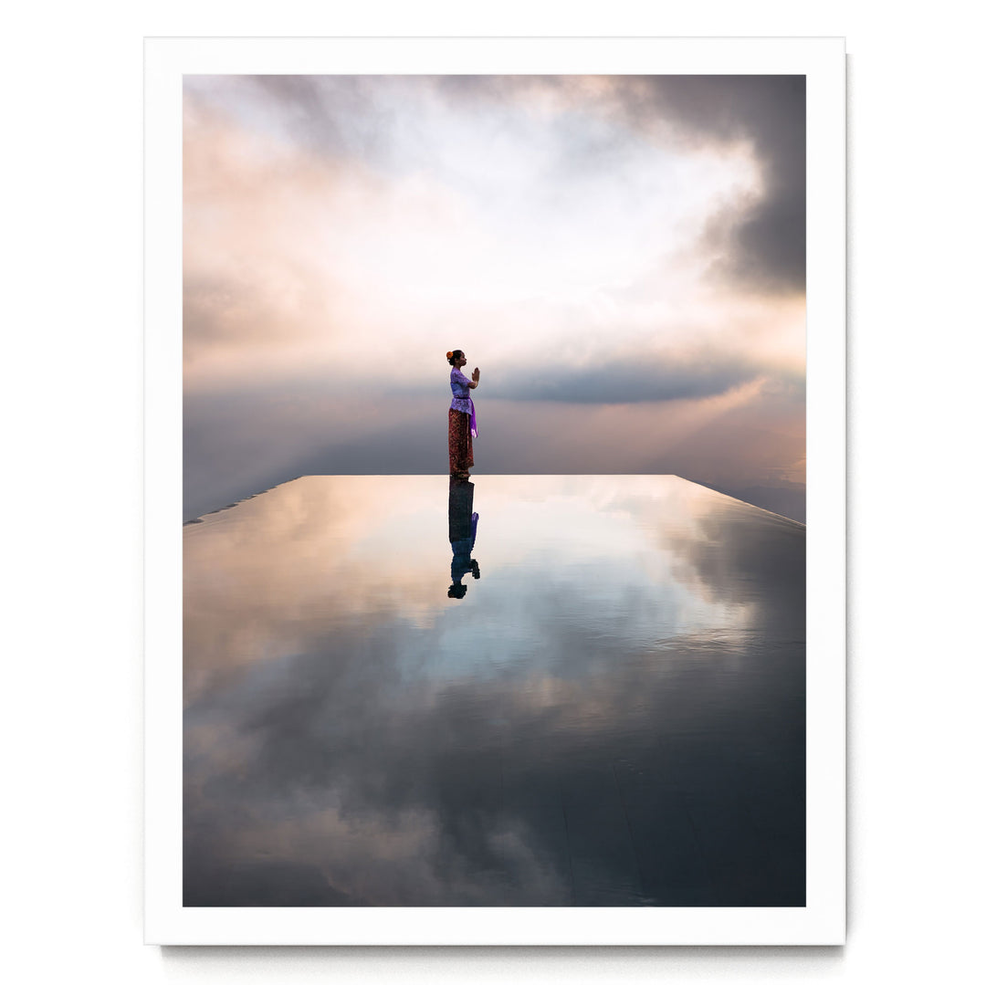 A person stands alone on a reflective surface, their reflection mirrored in the water below, against a backdrop of a cloudy sky.