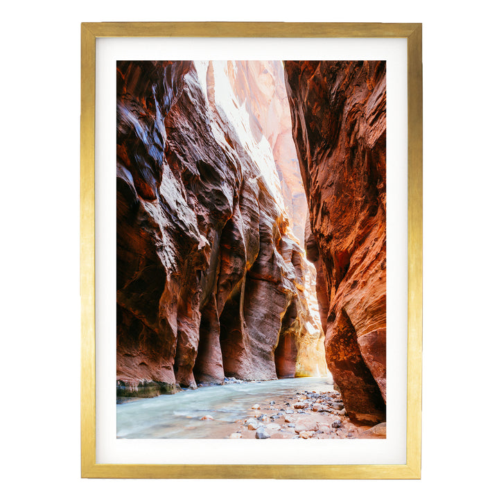 A framed photograph depicting a narrow, winding river flowing through a canyon with towering red rock walls.