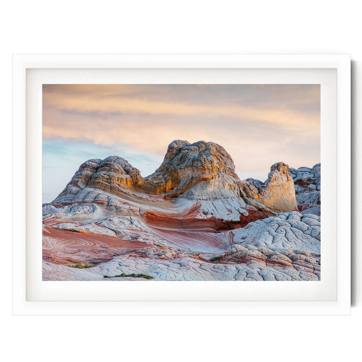 a striking natural landscape with a large, multi-layered rock formation in the foreground, set against a vibrant sky with a gradient of orange and pink hues.