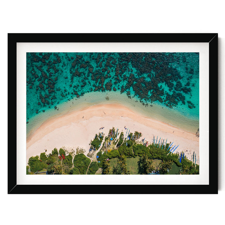 The image is an aerial view of a tropical beach with crystal clear turquoise waters, sandy shores, lush vegetation, and a few boats visible in the distance.
