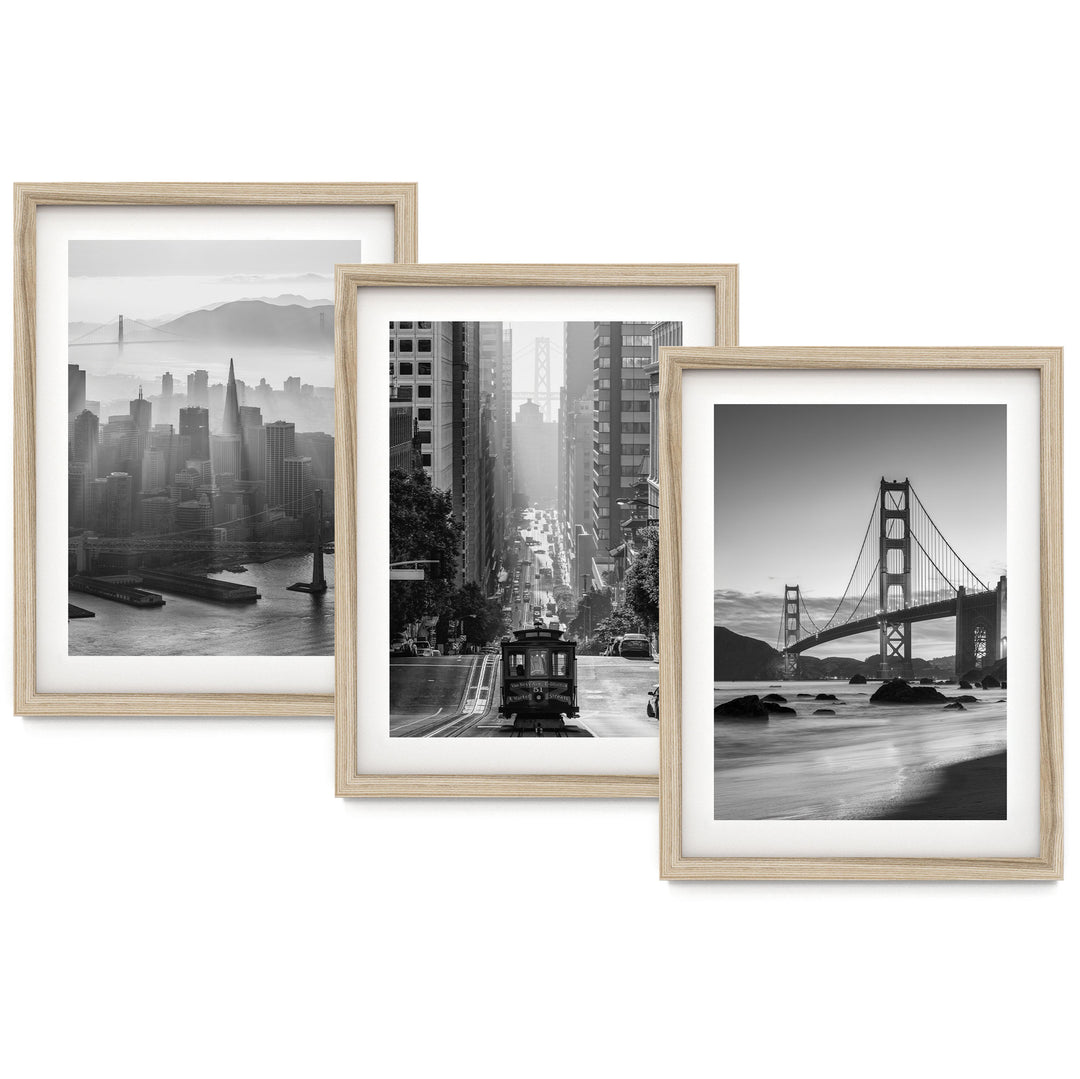 three framed black and white photographs of various city scenes, including a cityscape, a trolley car, and a bridge.