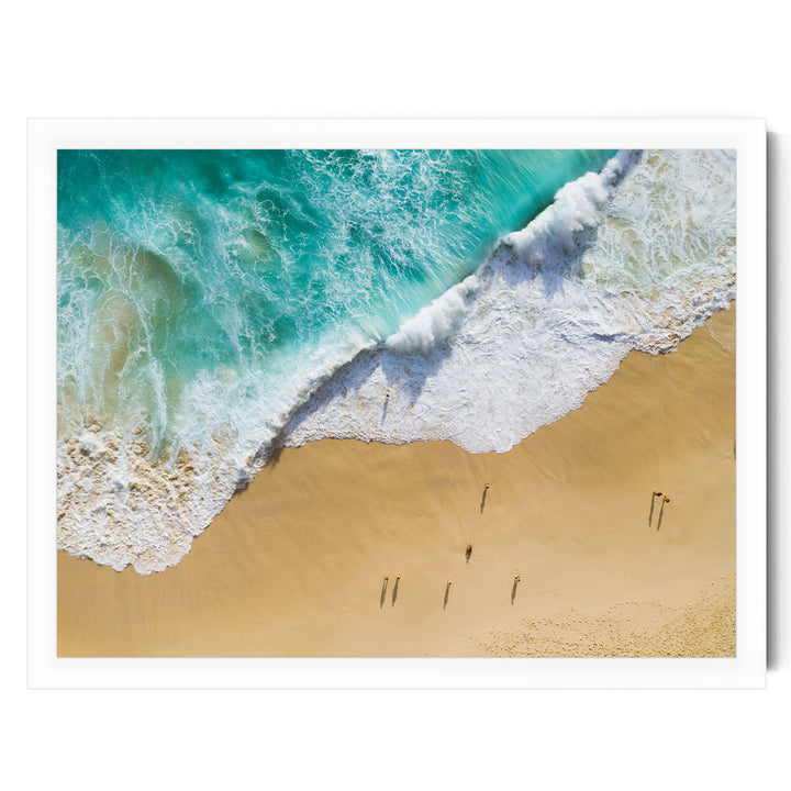 An aerial view of a beach with waves crashing onto the shore, and people walking along the sand.