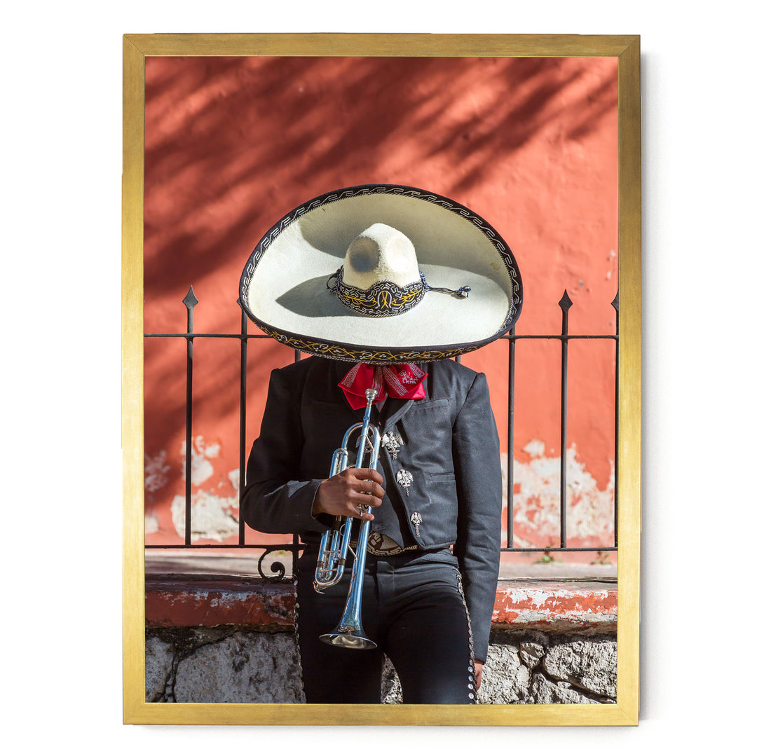 A person wearing a sombrero and a black jacket is playing a trumpet in front of a red wall.