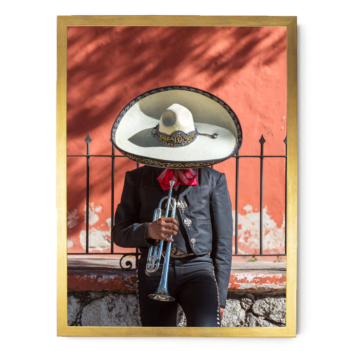 A person wearing a sombrero and a black jacket is playing a trumpet in front of a red wall.