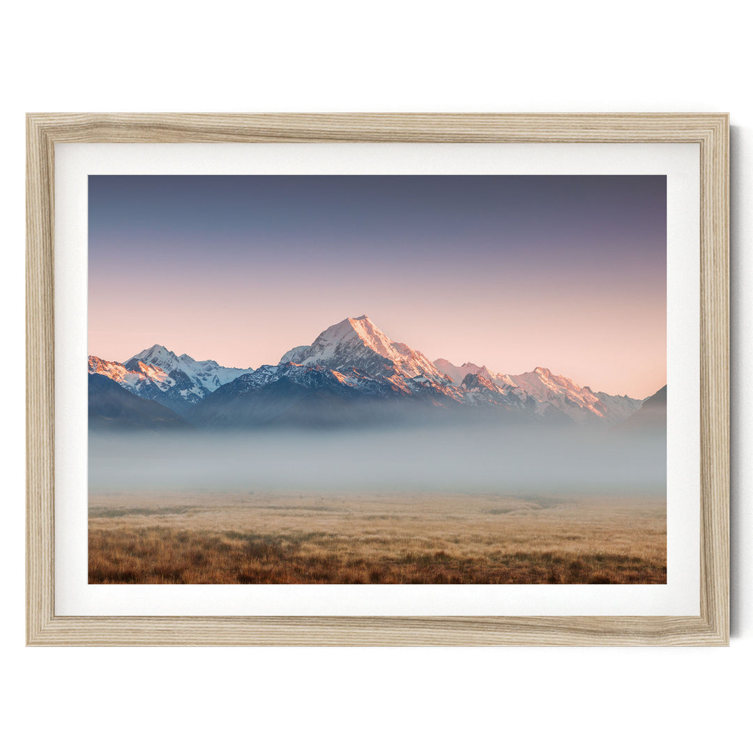 a breathtaking mountain range with snow-capped peaks against a vibrant sky, partially obscured by a hazy mist.