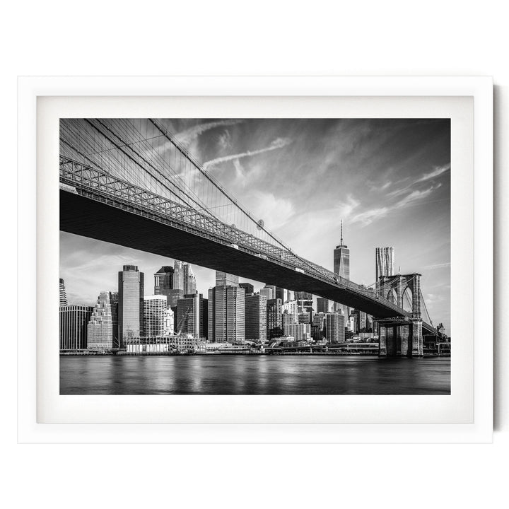 A black and white photograph of the Brooklyn Bridge spanning the East River, with the New York City skyline visible in the background.