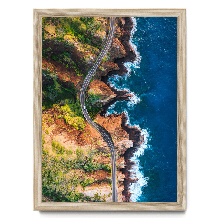 The image is an aerial view of a winding road cutting through a rugged, mountainous landscape with cliffs and rocky terrain.