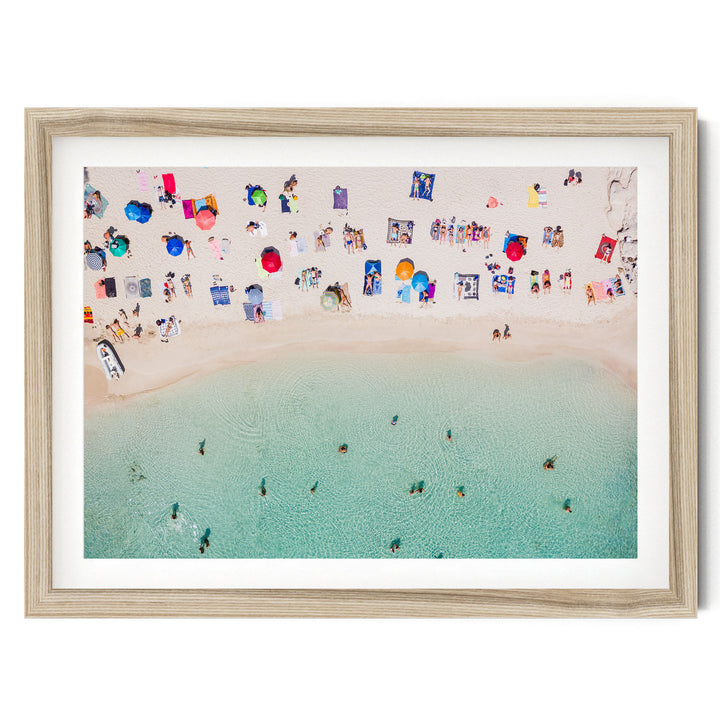 The image is an aerial view of a crowded beach with numerous people enjoying the sun, sand, and water.