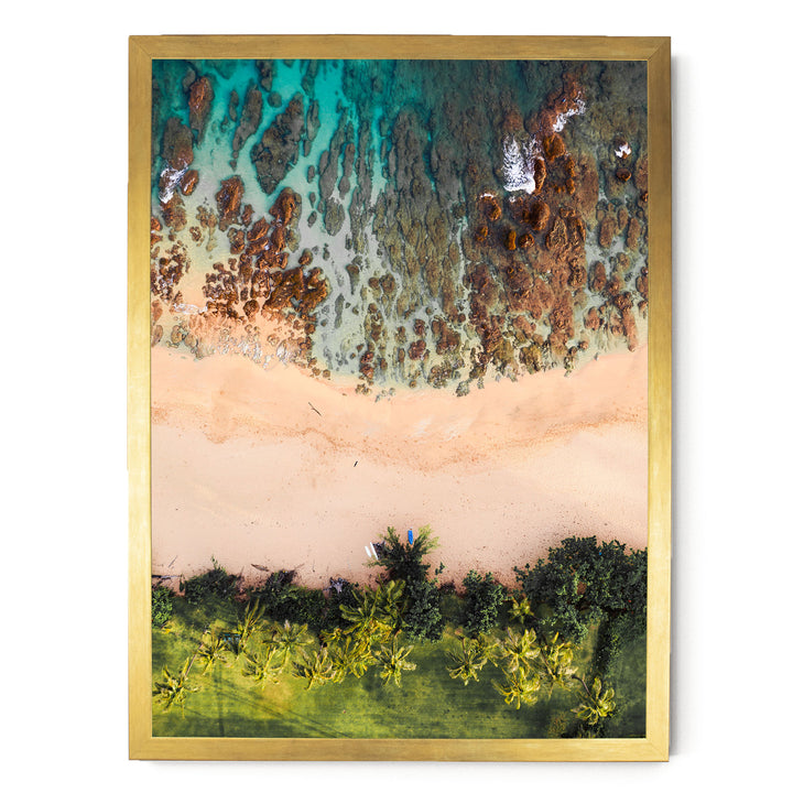 The image is a framed aerial view of a beach with a mix of rocky and sandy terrain, surrounded by lush greenery.