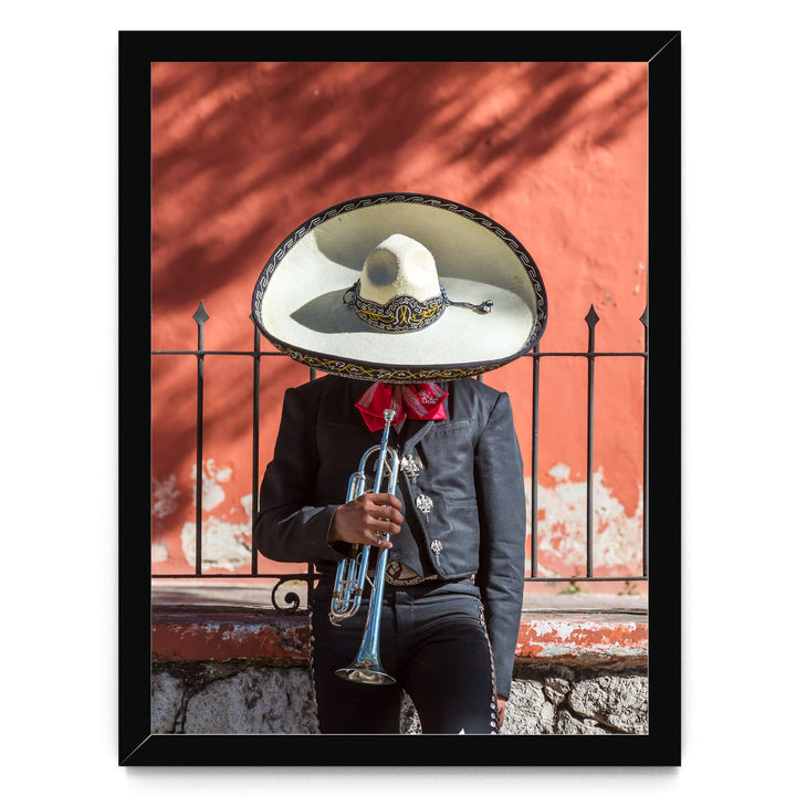 A person wearing a sombrero and a black jacket is playing a trumpet in front of a red wall.