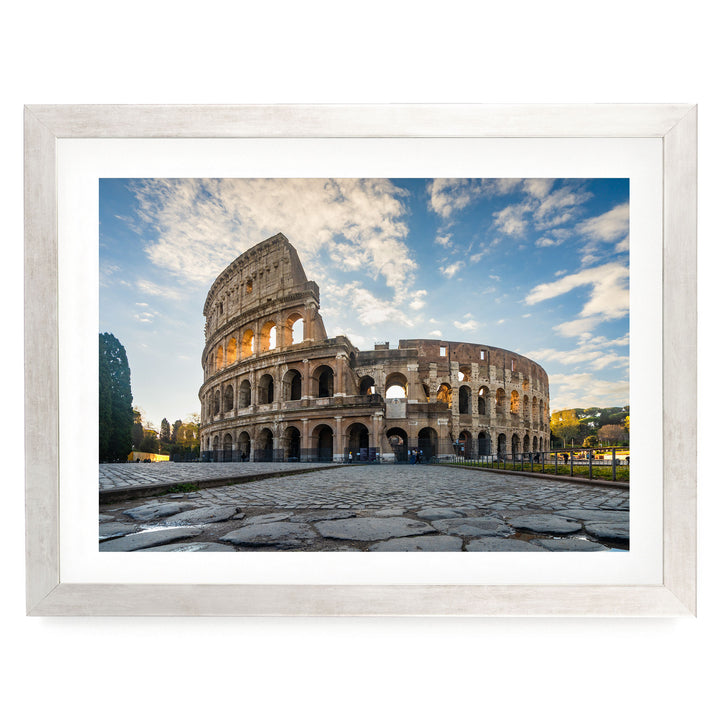 the Colosseum, an ancient amphitheater in Rome, Italy, with its distinctive oval shape and arches. The Colosseum is surrounded by a cobblestone courtyard, and the sky above is blue with some clouds.