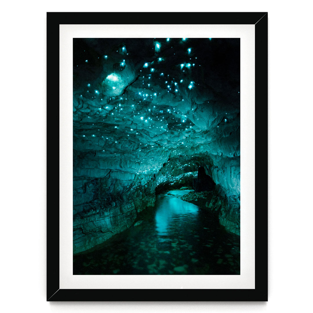 A framed photograph depicting a cave with a stream of water flowing through it, surrounded by glowing blue and green lights that create a mesmerizing, otherworldly atmosphere.