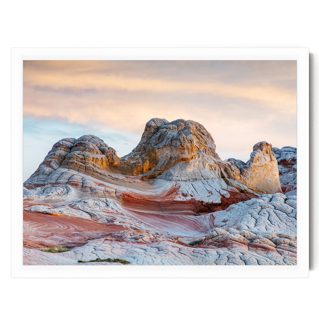 a striking natural landscape with a large, multi-layered rock formation in the foreground, showcasing a mix of orange, red, and white colors. The sky above is a beautiful gradient of orange and pink, creating a serene and picturesque backdrop for the scene.