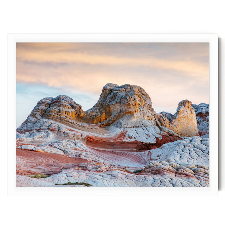 a striking natural landscape with a large, multi-layered rock formation in the foreground, showcasing a mix of orange, red, and white colors. The sky above is a beautiful gradient of orange and pink, creating a serene and picturesque backdrop for the scene.