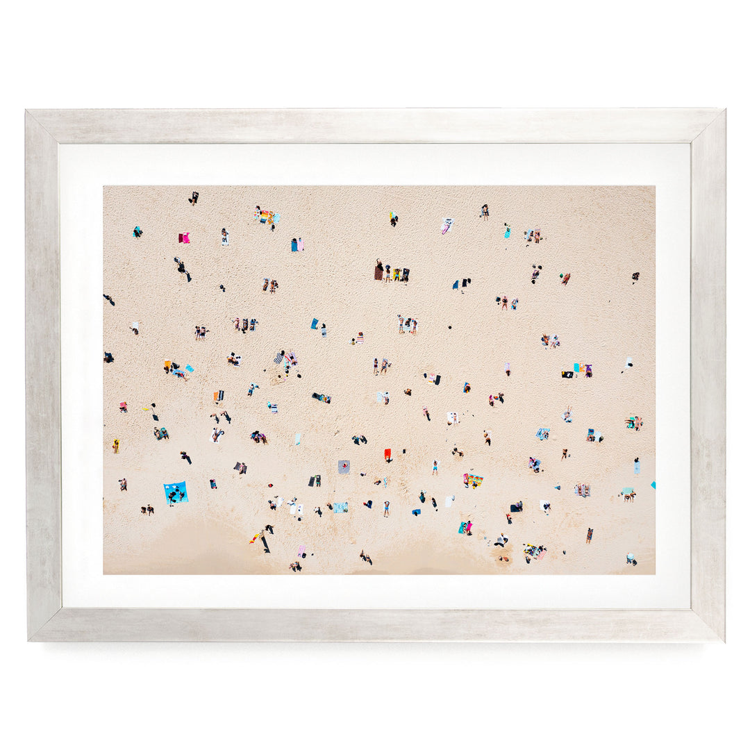 The image is a framed photograph depicting a beach scene with numerous people scattered across the sandy beach.