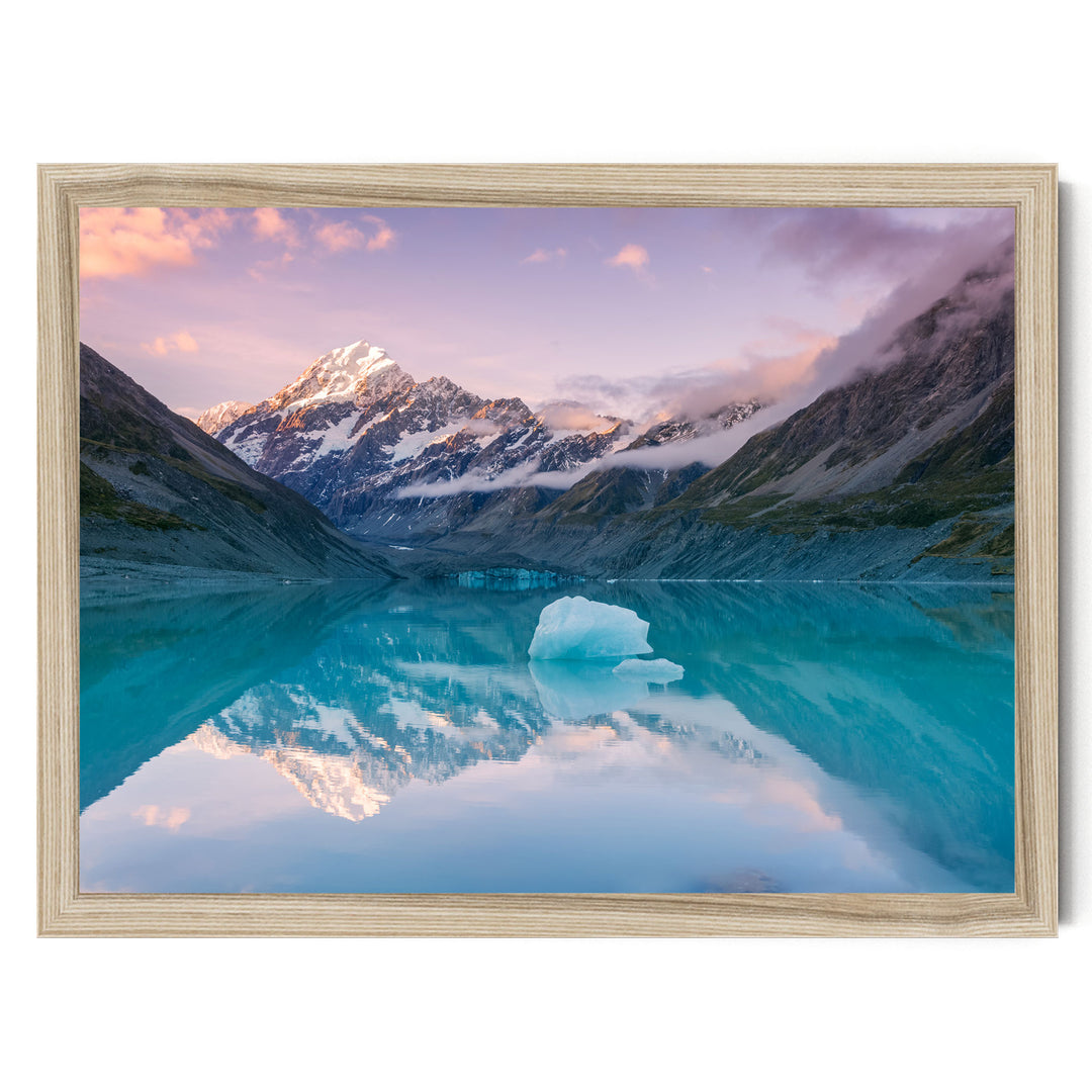 a serene mountain lake with a large ice formation in the center, surrounded by snow-capped peaks and a stunning sunset sky reflected in the calm waters.