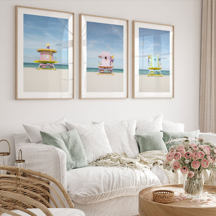 a living room with a white sofa, a wicker chair, and three framed beach scenes on the wall.
