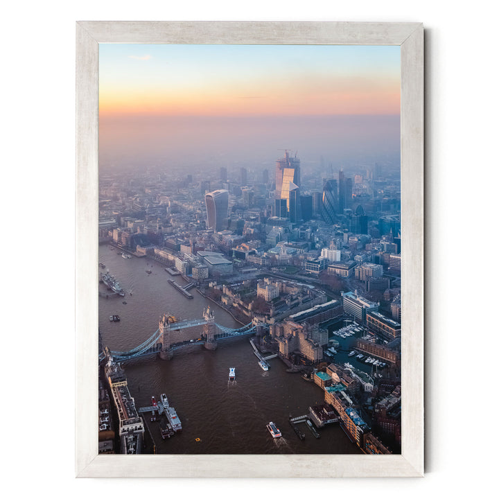 The image is an aerial view of a cityscape with a river running through it, featuring a bridge and several boats. The city is densely populated with tall buildings, and the sky is painted in warm hues of orange and pink, suggesting either sunrise or sunset.