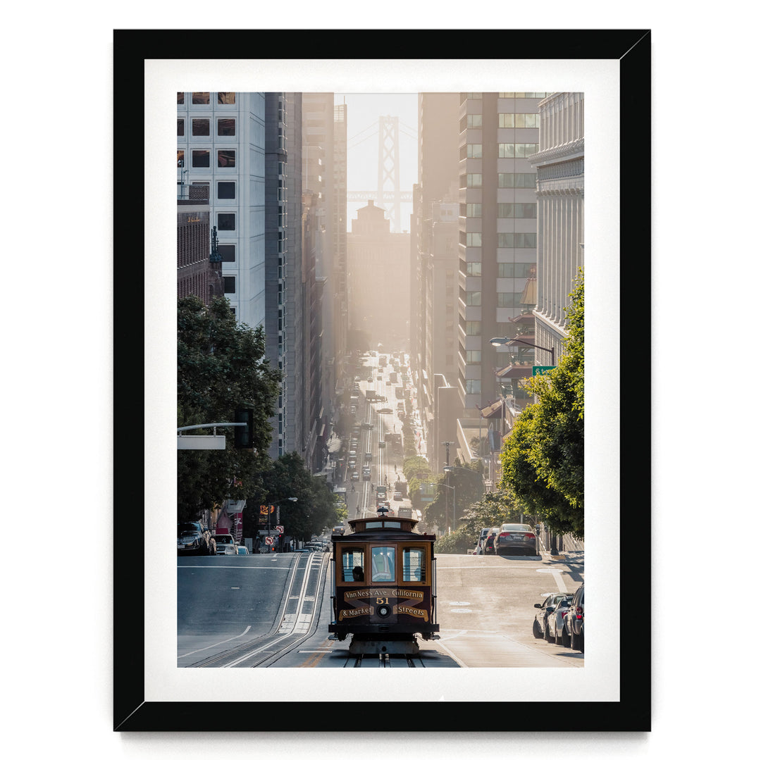 A framed photograph depicting a trolley car traveling down a city street, surrounded by tall buildings and trees.
