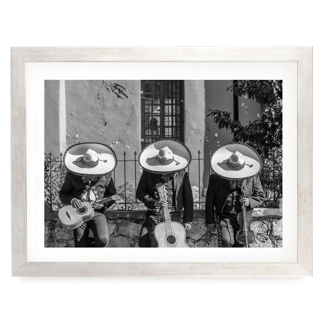 A black and white photograph of three men wearing sombreros and playing musical instruments, such as guitars and drums, in front of a building.