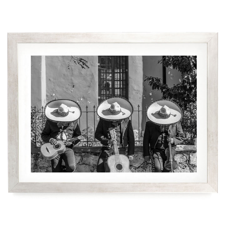A black and white photograph of three men wearing sombreros and playing musical instruments, such as guitars and drums, in front of a building.