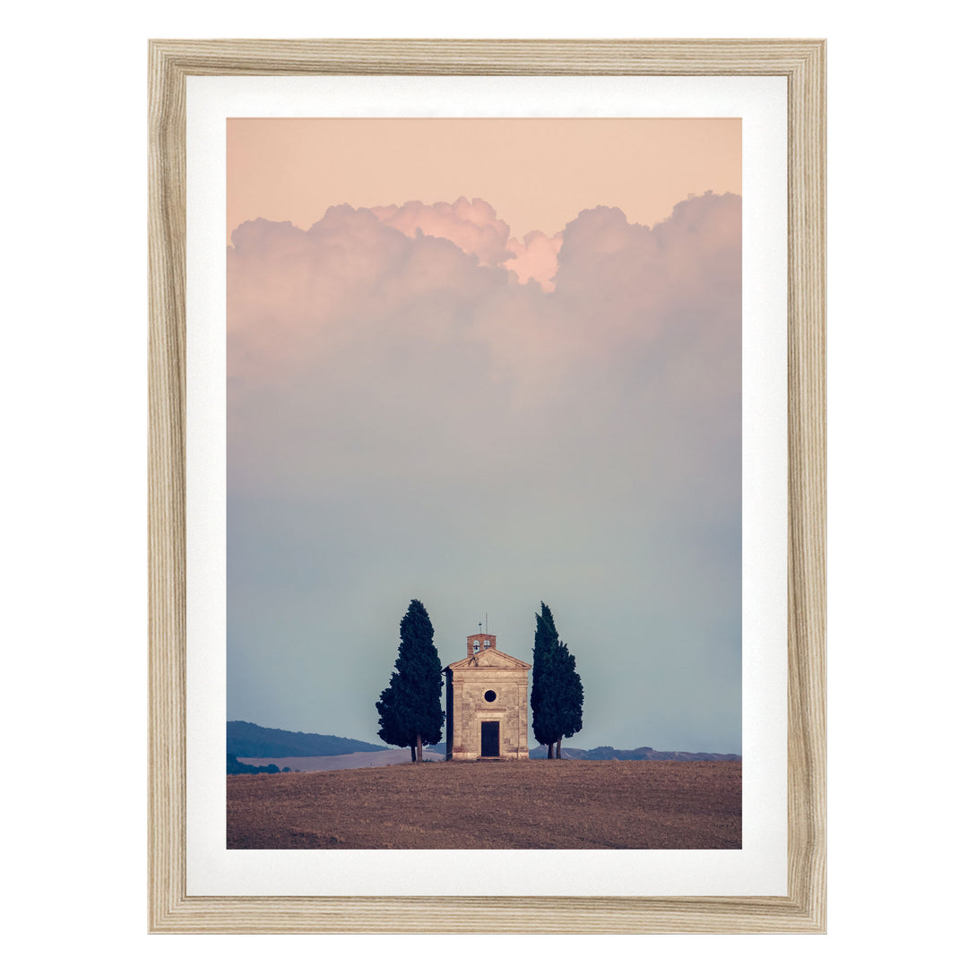 A framed photograph depicting a small stone church with a bell tower, surrounded by trees, set against a cloudy sky.
