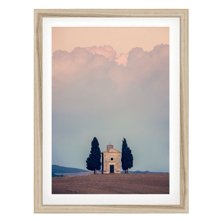 A framed photograph depicting a small stone church with a bell tower, surrounded by trees, set against a cloudy sky.