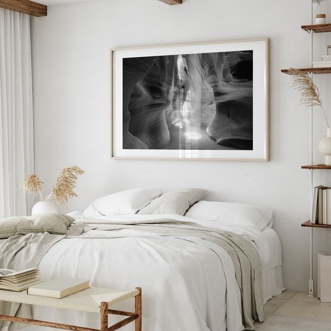 a serene and minimalist bedroom with a large black and white photograph of a canyon or rock formation hanging on the wall above a bed with white bedding.