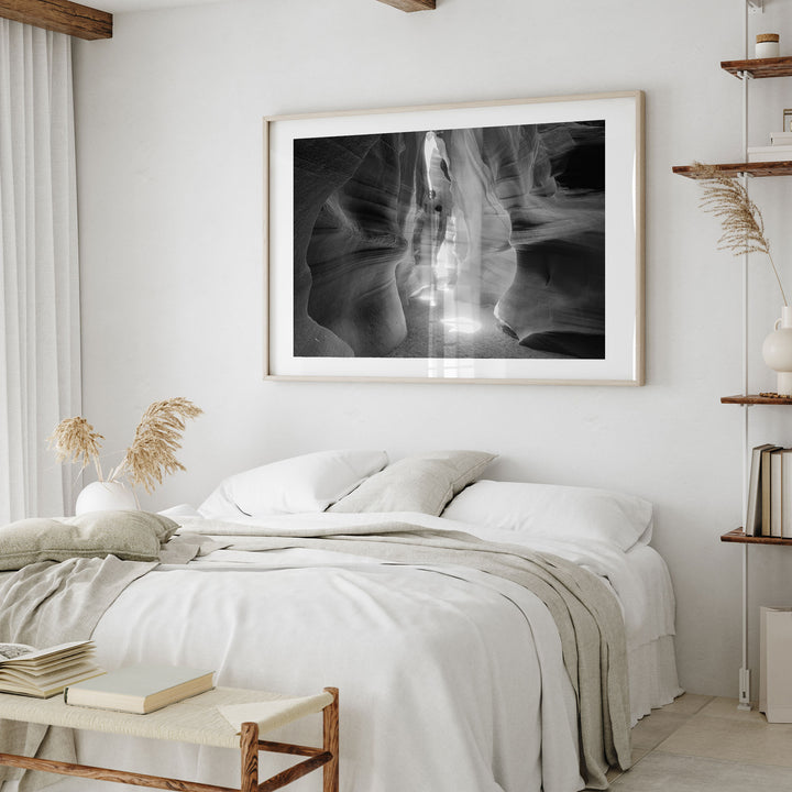 a serene and minimalist bedroom with a large black and white photograph of a canyon or rock formation hanging on the wall above a bed with white bedding.