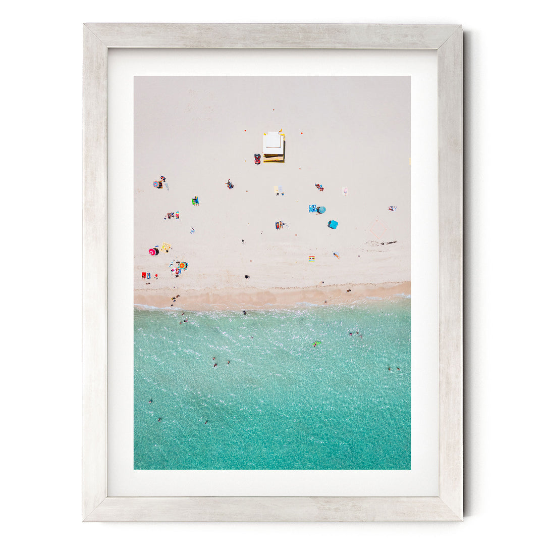 The image is a framed photograph depicting a beach scene with people enjoying the sun and water.