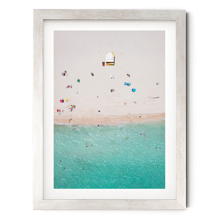 The image is a framed photograph depicting a beach scene with people enjoying the sun and water.