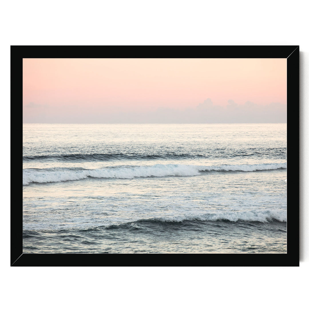 A serene ocean scene with gentle waves lapping against the shore, set against a soft pink and orange sky.