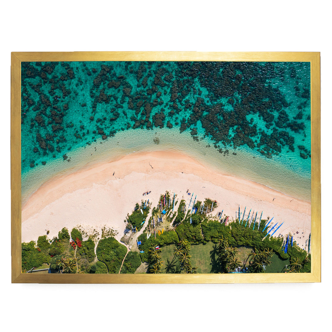 The image is an aerial view of a tropical beach with a clear turquoise ocean, a sandy beach, and lush vegetation surrounding the shoreline.
