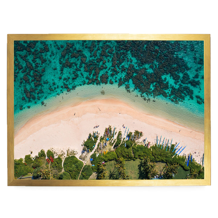 The image is an aerial view of a tropical beach with a clear turquoise ocean, a sandy beach, and lush vegetation surrounding the shoreline.