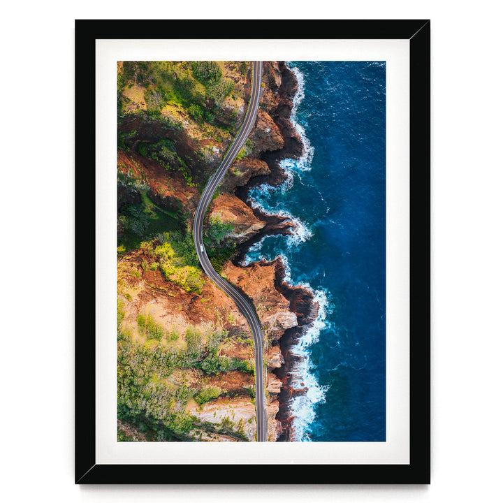 An aerial view of a winding coastal road cutting through a rugged, rocky coastline with crashing waves.